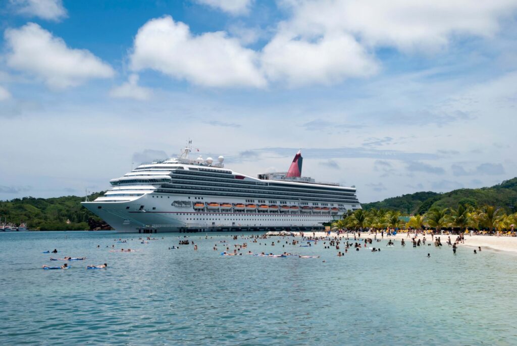 Bay beach crowded with tourists from the cruise ship moored nearby